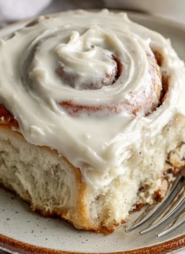 Freshly baked cinnamon rolls topped with creamy icing on a wooden surface.