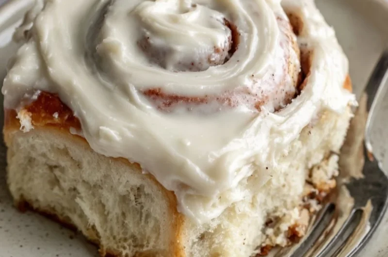 Freshly baked cinnamon rolls topped with creamy icing on a wooden surface.