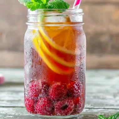 A refreshing glass of Earl Grey Raspberry Iced Tea with raspberries and lemon slices.