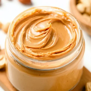 Homemade peanut butter spread in a jar with peanuts on the side.