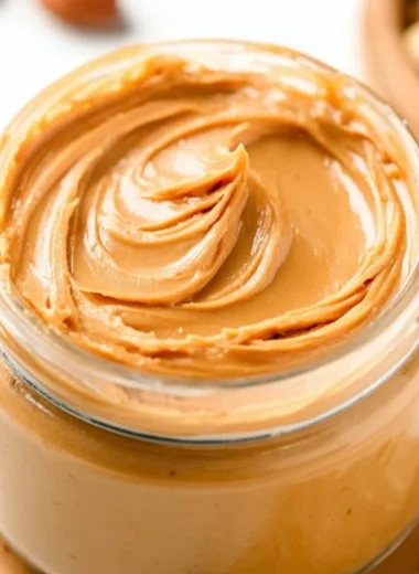 Homemade peanut butter spread in a jar with peanuts on the side.