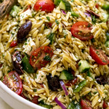 A vibrant bowl of cozy Greek Orzo Salad with vegetables and feta cheese.