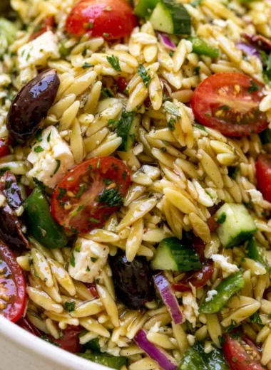 A vibrant bowl of cozy Greek Orzo Salad with vegetables and feta cheese.