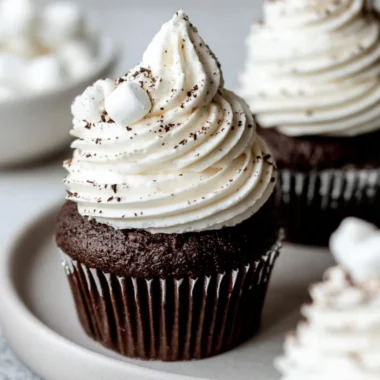 Hot chocolate cupcakes topped with marshmallow buttercream on a wooden table.