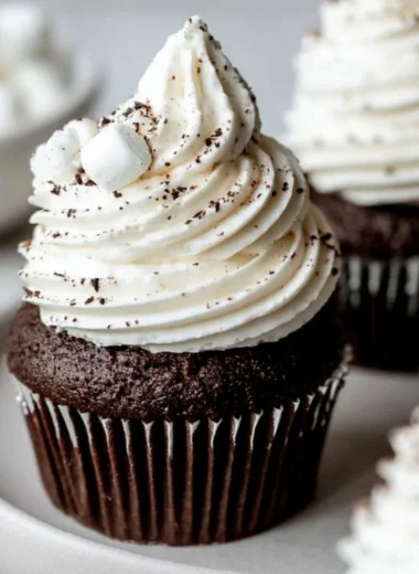 Hot chocolate cupcakes topped with marshmallow buttercream on a wooden table.