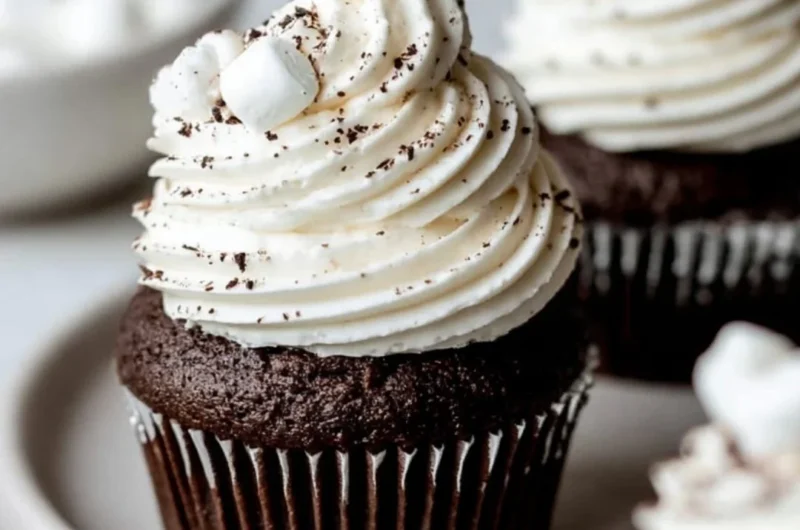 Hot chocolate cupcakes topped with marshmallow buttercream on a wooden table.